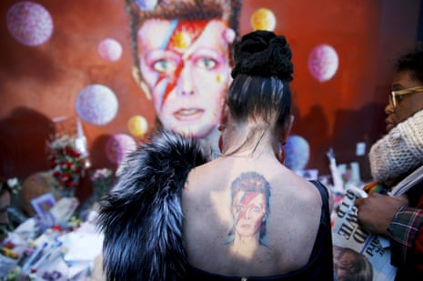 A woman with a Ziggy Stardust tattoo visits a mural of David Bowie in Brixton