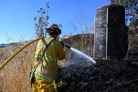 A firefighter pouring water on scarred vegetation.