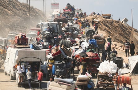 People and their possessions, some in or on vehicles, fill a road