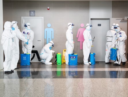 People in full white hazmat suits with goggles carrying large spray canisters