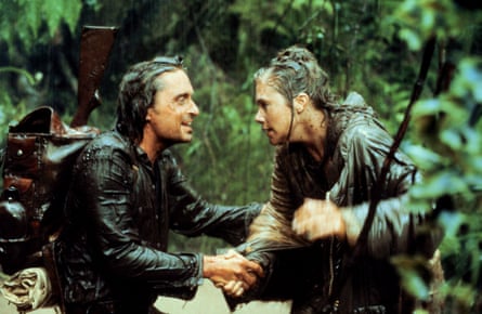 A man and woman look at each while drenched by rain in the jungle.