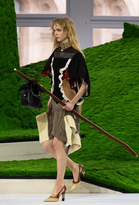 Model carries staff with handbag hooked on to the end.