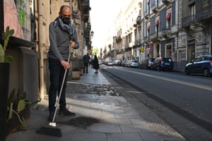 A store owner sweeps up ash that fell on Tuesday during an eruption of Mount Etna