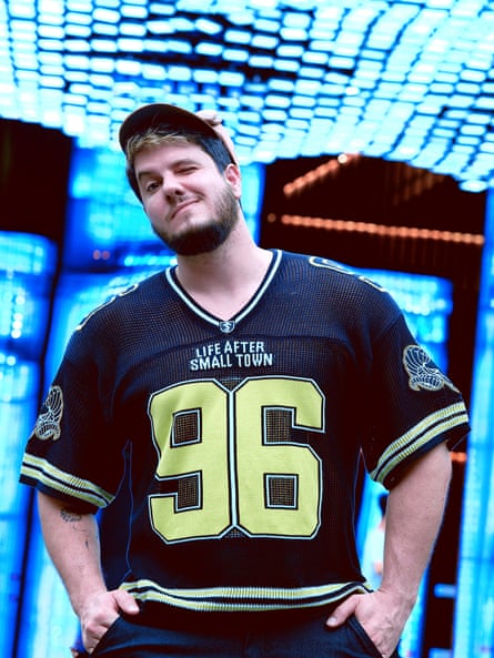 A man wearing an American football shirt and cap, hands in pockets, winking