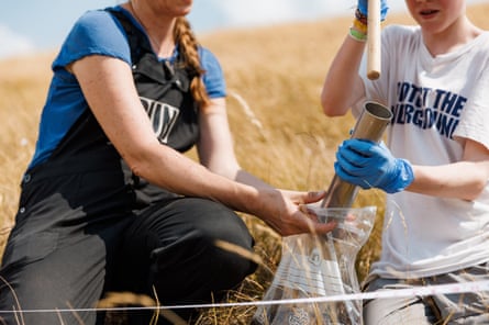 Two women on a grassy hillside poke the soil sample out of a tube into a plastic bag