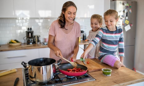 Woman cooking food on a gas hob cooker in a kitchen with two twin girls