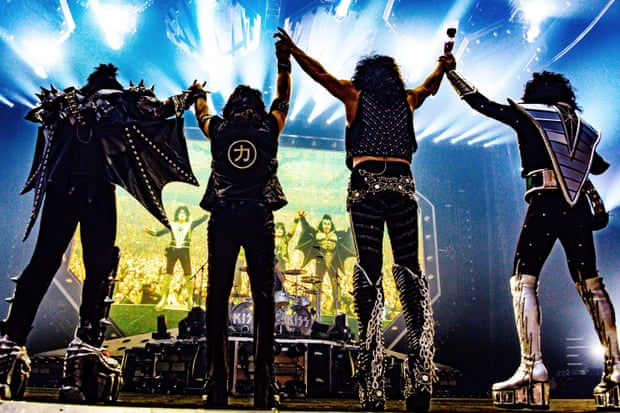 The four members of the band kiss hold hands and jump in the air while on stage in Sydney as lights flash in the background