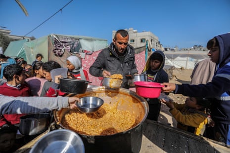People displaced by Israeli strikes line up to receive food cooked in large pots and distributed for free in Rafah, Gaza on January 20, 2024.