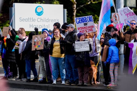 People wave signs to passing cars during a rally outside of Seattle Children’s Hospital