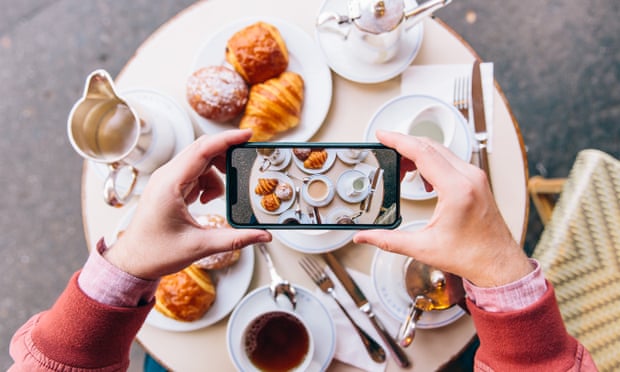 A smartphone taking a snap of a table of tea and pastries