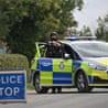 A police officer stands by a car blocking a road, with a sign saying: 'Police. Stop'