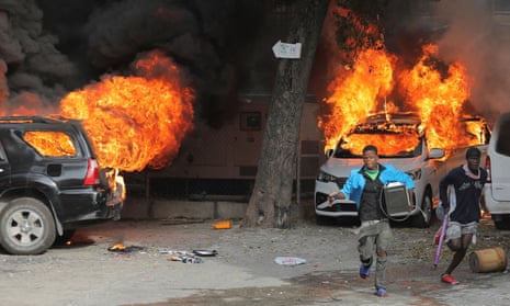 Men run with looted goods near cars on fire during protests over rising fuel prices and crime in Port-au-Prince on Wednesday.