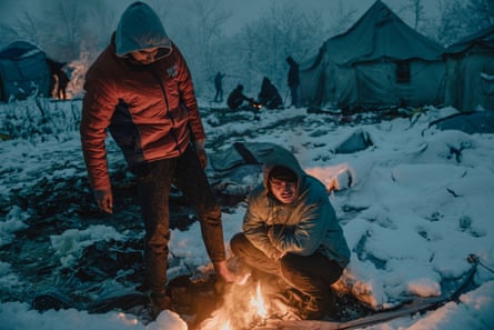 Two people gather around the fire amid snow