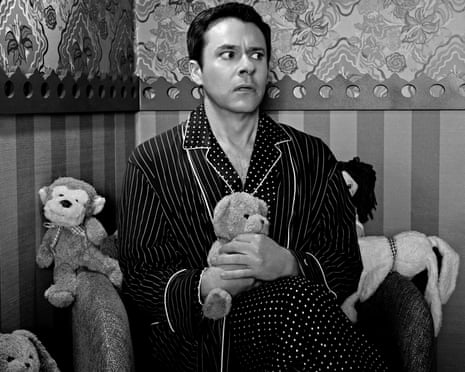 A black and white image of Bryan Safi in pyjamas and dressing gown clutching a teddy bear, looking worried.