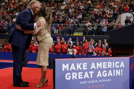 Man in blue suit and woman in beige Gucci set hug on stage as people in crowd clap