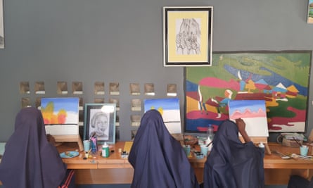Three girls wearing navy blue hijabs paint landscapes with their backs to the camera