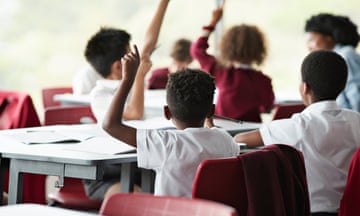 Pupils, seen from behind, raise their hands in a classroom