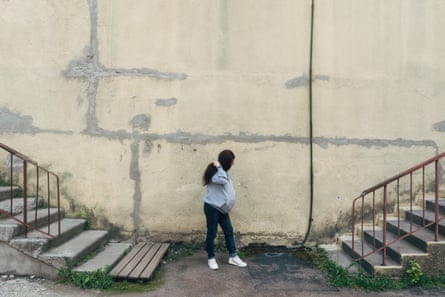 Yulia, standing in front of a blank wall, flights of steps on either side, her hair obscuring her face.