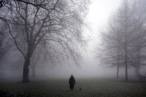 A woman walking her dog emerges from the fog in Parsons Green, west London