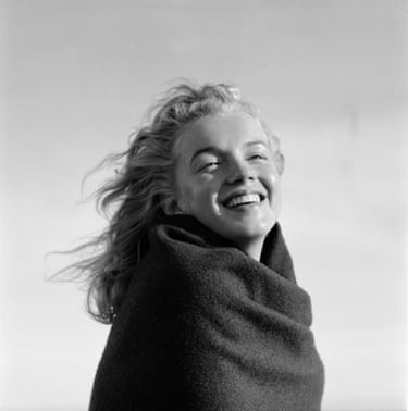 Marilyn Monroe poses with a big smile while looking into the distance in a black and white image