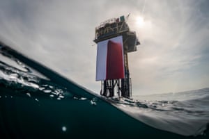 A large piece of fabric with what looks like blood on it is unfurled from a tall oil rig in the middle of the sea