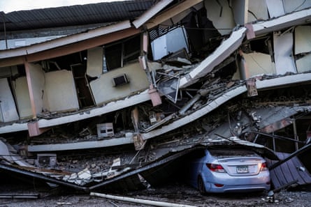 A car sits crushed beneath debris from a collapsed building