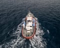 An aerial view shows a white boat with red trim moving through dark water, creating a wake.