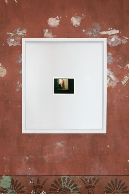 A small pPolaroid of a man standing nude next to a white doorway, framed and hung on a wall.