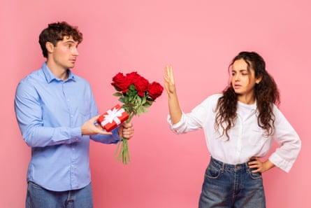 Displeased European lady rejecting her boyfriend with roses and gift on Valentine’s Day, man giving present to his girlfriend, pink studio background