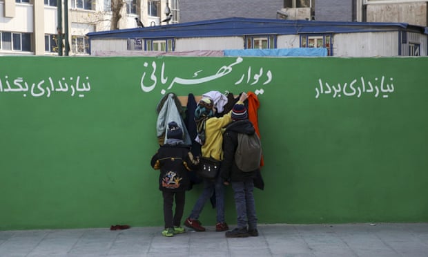 Youths check clothes hung on hooks at a ‘wall of kindness’ next to an underground station in central Tehran