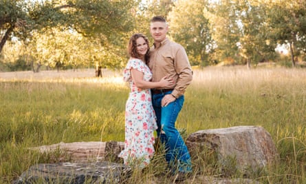 man and woman standing in a meadow. man wears jeans and beige shirt, woman wears flowery dress