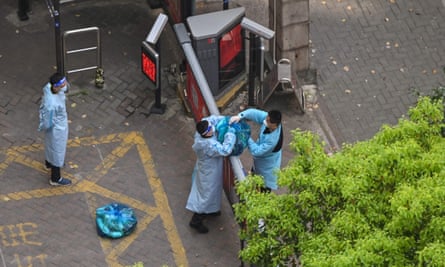 View from above of a man handing a bag of supplies over a high gate to another man on the other side, both in full PPE