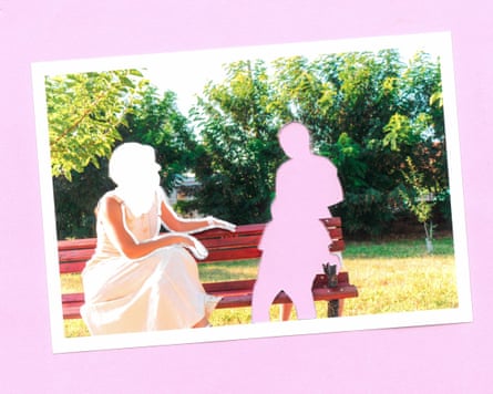 A woman sits on a bench in a park and gestures towards two children, one sitting on the bench and other standing behind it. Their faces have been obscured