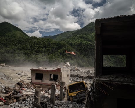 In Betrawati, Nepal, a rescue helicopter flies over flood debris and a damaged building
