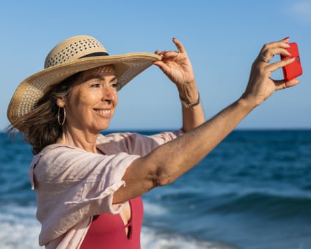 Senior woman taking a selfie on the beach with straw hat
