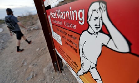 In this Tuesday, July 24, 2018 photo, a hiker walks past a heat warning sign at sunrise, in Phoenix.