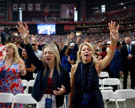 two women singing with arms raised inside venue