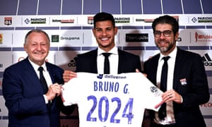 Bruno Guimarães sostiene la camiseta de Lyon junto al presidente del club Jean Michel Aulas y el director Juninho.