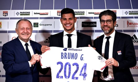 Bruno Guimarães holds the Lyon shirt alongside club president Jean Michel Aulas and director Juninho.