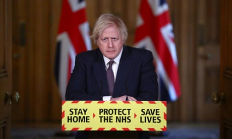 Boris Johnson stands at a lectern with a sign on the front sasying: Stay home, protect the NHS, save lives