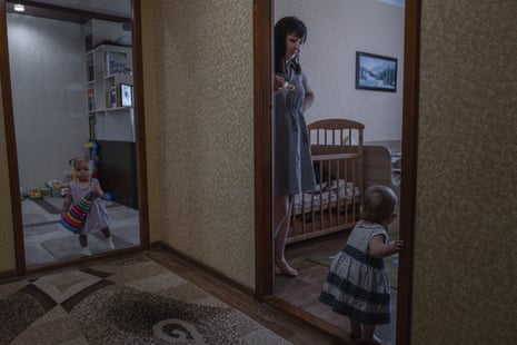 A woman in an apartment looks after two toddler girls who have just started walking 