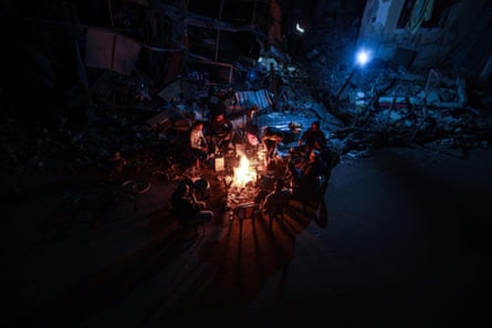 Night shot from a high vantage point looking down at a group of Palestinians sitting around a fire in the rubble of Khan Younis, Gaza Strip.
