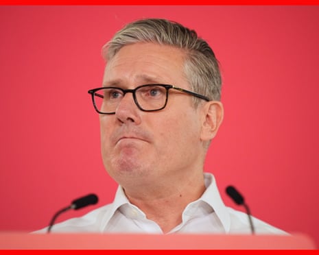 Starmer in black-rimmed glasses and white shirt at a table with microphones against a red backdrop.
