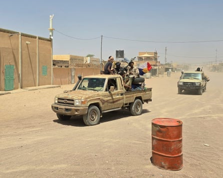 Armed men ride through a desert town on the back of a flatbed truck