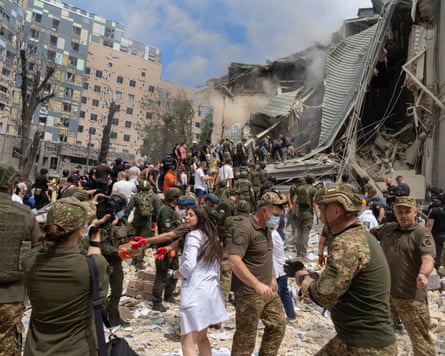 Soldiers, medical workers and volunteers clamber over a large pile of rubble in front of a collapsed building