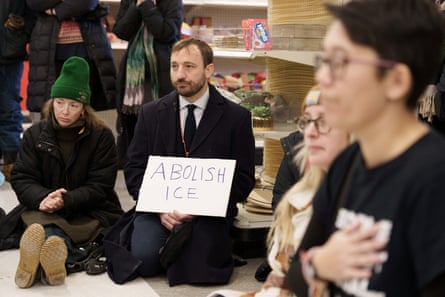 A circle of people sitting and kneeling in a store, with a man in a suit holding a sign that says Abolish ICE.