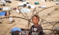 A child stands behind barbed-wire along a slope near a camp housing displaced Palestinians in Rafah in the southern Gaza Strip.