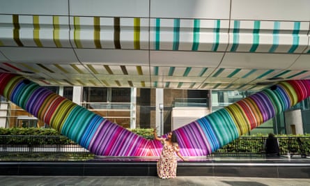 An art installation of large Pride-striped ducts with a women in front taking a selfie