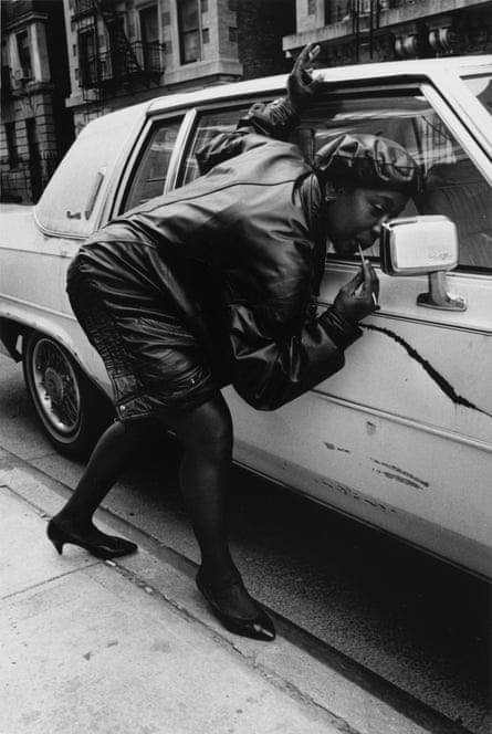 A woman stoops to do her makeup in a car wing mirror