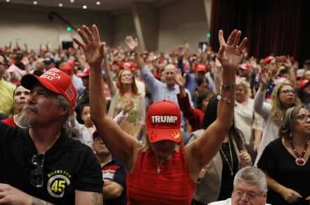 a woman with her head down and arms raised wearing a red cap in a room full of people